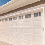 A light-colored garage door with windows on a home with beige siding and natural stone in sunny weather.