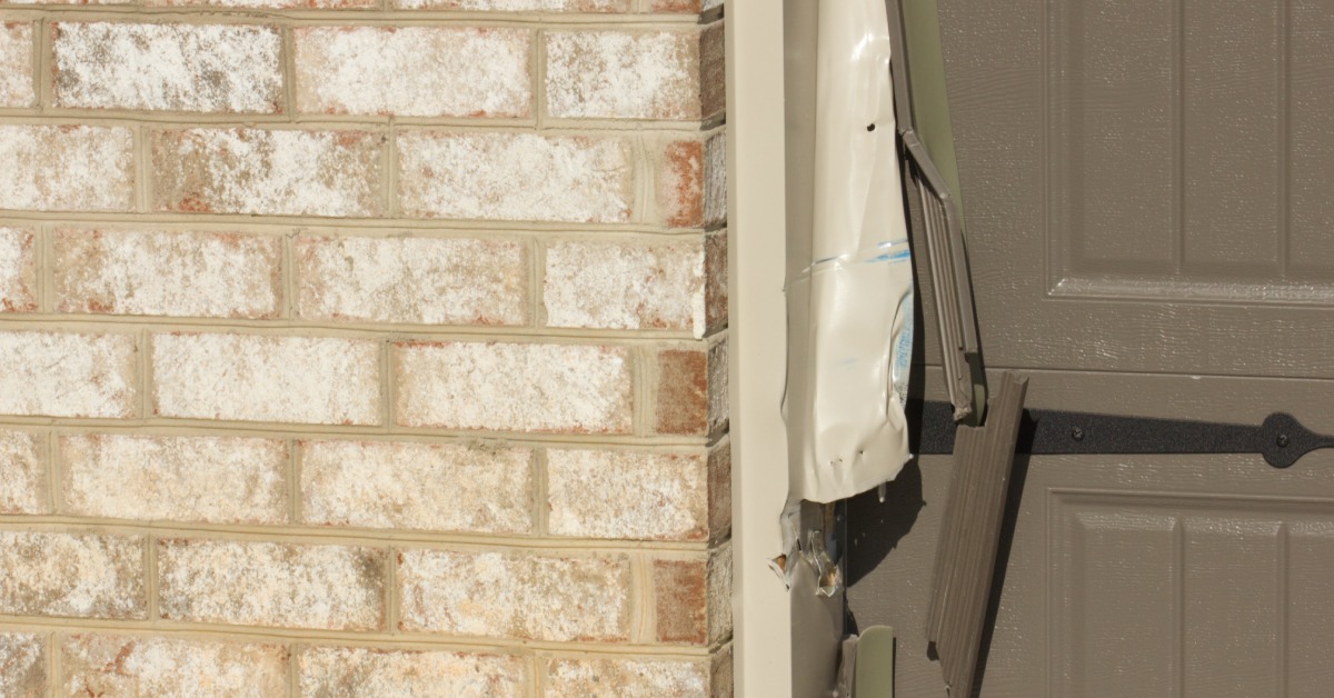 A close-up of the side of a brown garage door where a car has left a damaged impact on the door and frame.