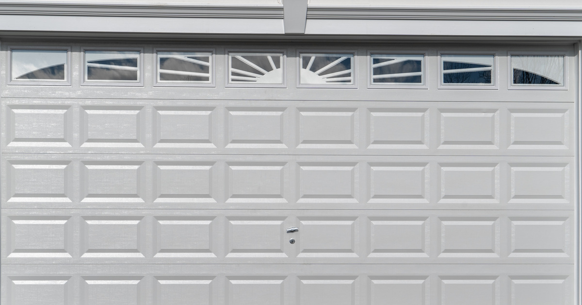 A white double car panel garage door is framed with white trim and features transom windows divided by muntins.
