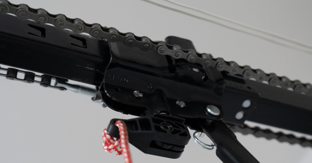 A black chain wraps around both sides of a black metal track with a plastic tab holding a red and white braided rope.