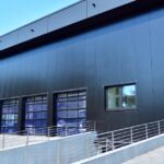 A navy-blue warehouse features five built-in frameless garage doors with vehicles visible through the glass.