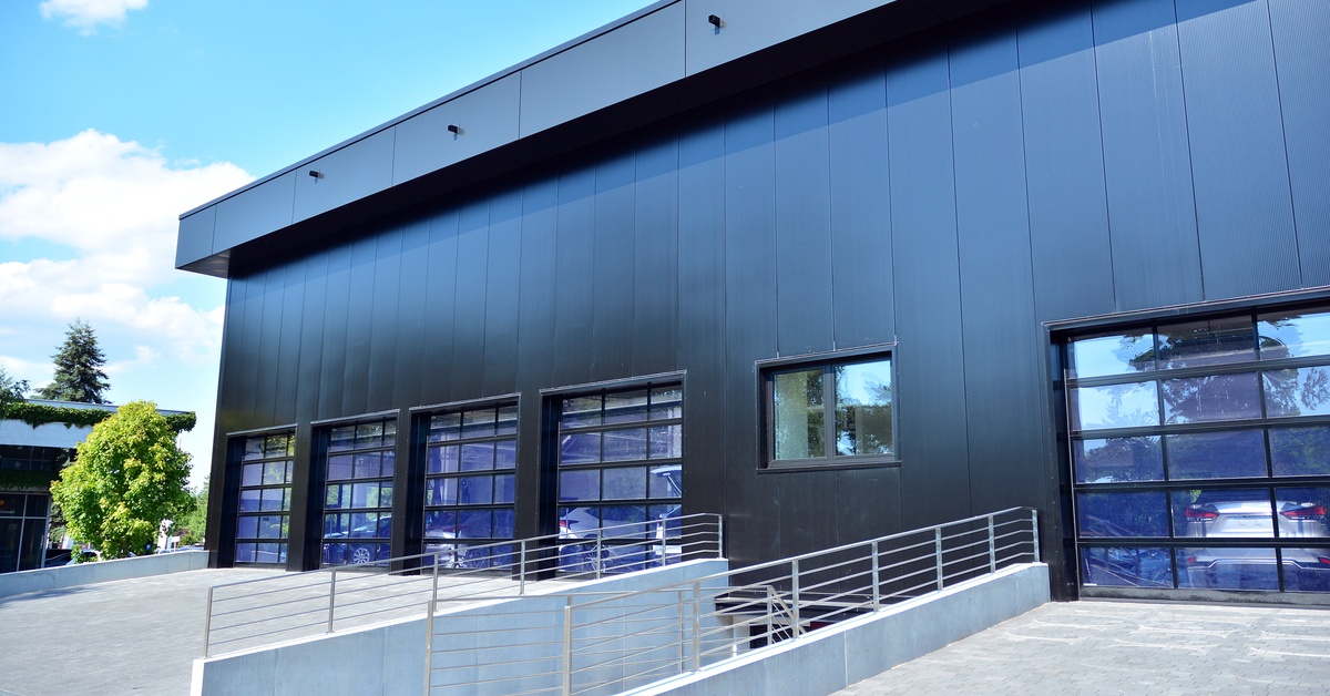 A navy-blue warehouse features five built-in frameless garage doors with vehicles visible through the glass.