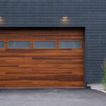 A faux wood garage door featuring horizontal frosted windows. Tall green plants border the door and concrete driveway.