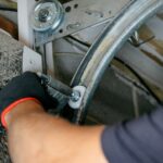 A close-up view of a garage door repair man wearing black gloves fixes the rollers on a home's garage door.