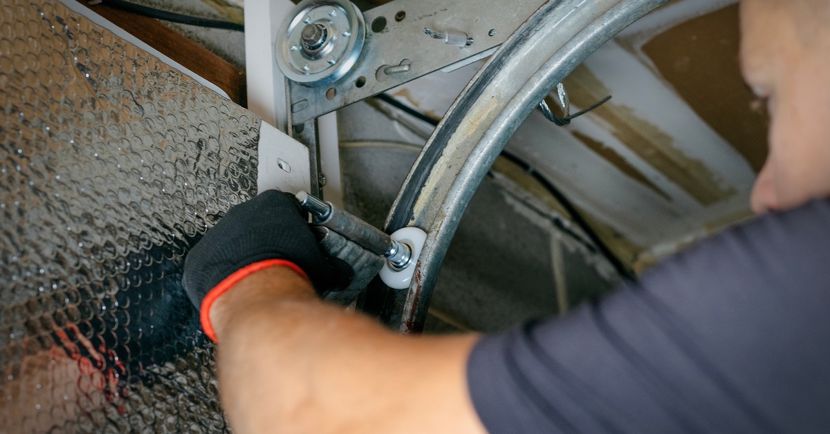 A close-up view of a garage door repair man wearing black gloves fixes the rollers on a home's garage door.
