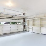 The inside of a modern garage with a white sectional garage door. The garage has empty white cabinets along the wall.