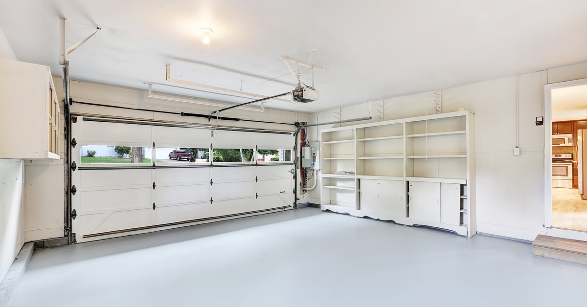 The inside of a modern garage with a white sectional garage door. The garage has empty white cabinets along the wall.