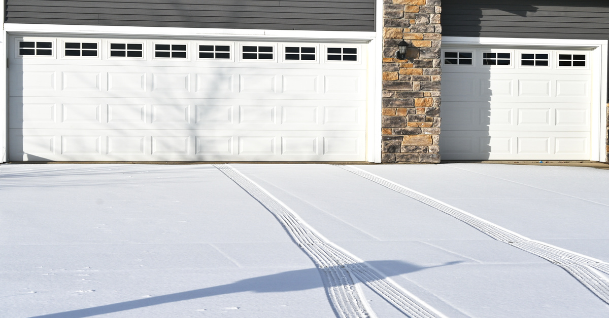 The front of two white garage doors on a home. The driveway is covered in snow, with tire tracks coming from the garage door.
