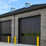 A modern industrial building contains three dark brown garage doors with four windows near the bottom.