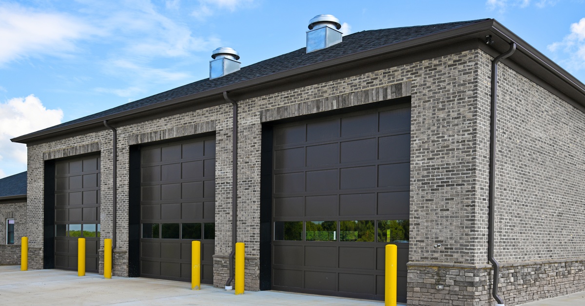 A modern industrial building contains three dark brown garage doors with four windows near the bottom.