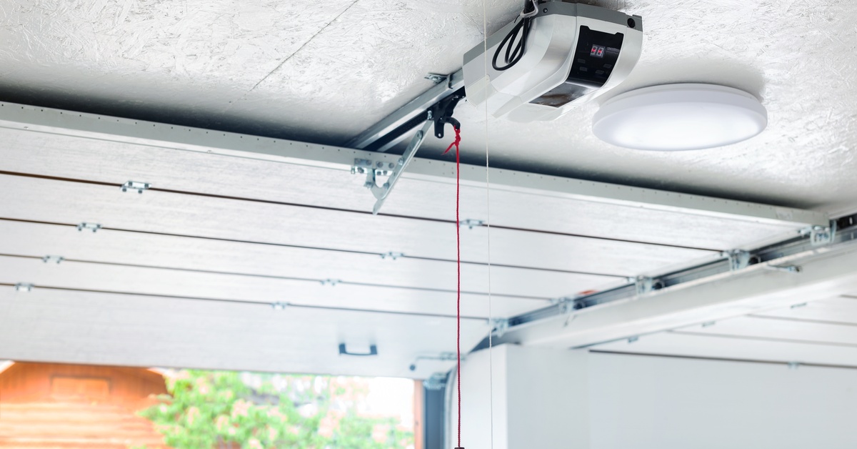 A modern garage interior contains a mounted garage door opener with a red emergency cord and metal track.