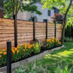 A modern wooden fence contains horizontal cedar slats and black posts, fronted by vibrant marigolds and lush greenery.
