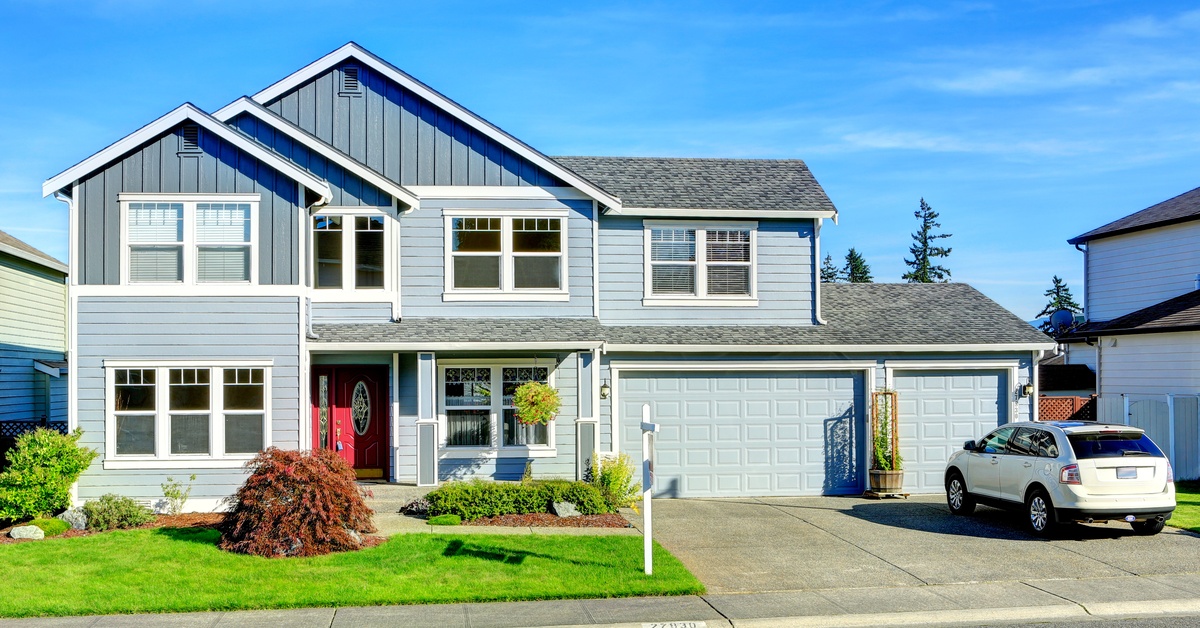 A two-story gray suburban home contains double garage doors, a red front door, green lawn, and white SUV in the driveway.