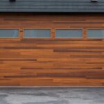 A modern brown wooden garage door with four frosted glass windows sits against a dark gray home exterior.