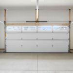 A clean two-car garage contains a white sectional door with windows, an overhead opener, and a concrete floor.