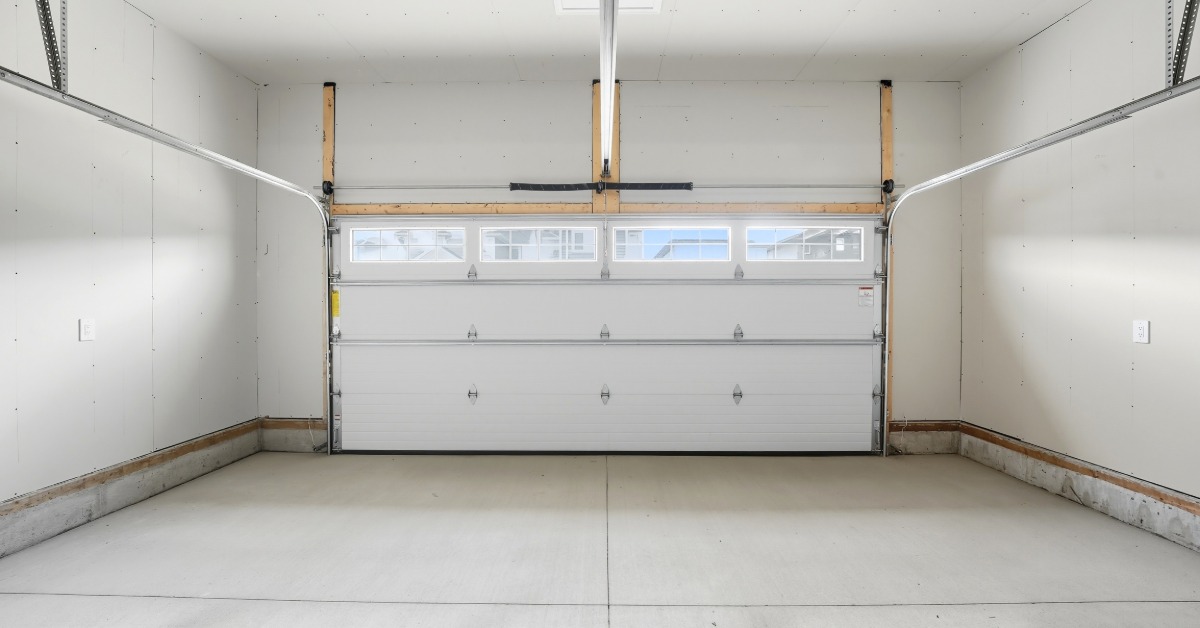 A clean two-car garage contains a white sectional door with windows, an overhead opener, and a concrete floor.