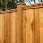 A natural wood privacy fence with vertical boards and decorative post caps extends across a backyard.