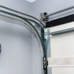 A white garage door follows a curved metal rail system around a corner next to a wall-mounted round light.