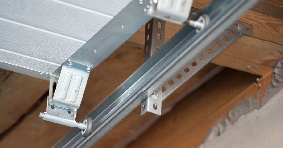 A garage door roller moves along a metal track beneath the sectional door, with support brackets mounted to the ceiling.