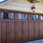 A brick home features a brown wooden garage door with upper windows beneath a beige gable and an exterior lantern.