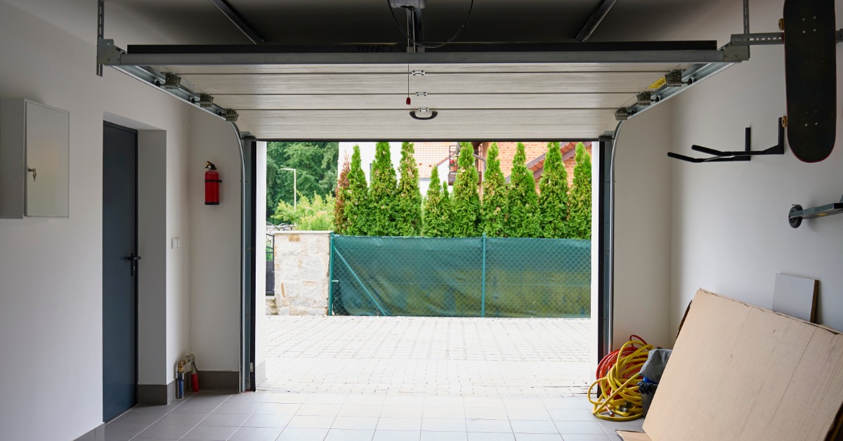 Interior view of a residential garage with an open overhead garage door, visible tracks, and a tiled floor.
