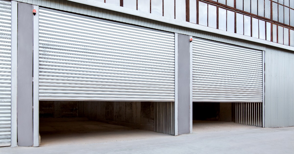Two partially open silver rolling steel doors on the exterior of a commercial warehouse, revealing spacious storage areas inside.